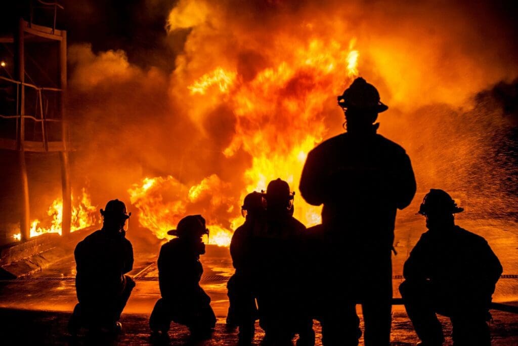 A group of firefighters standing in front of a fire.