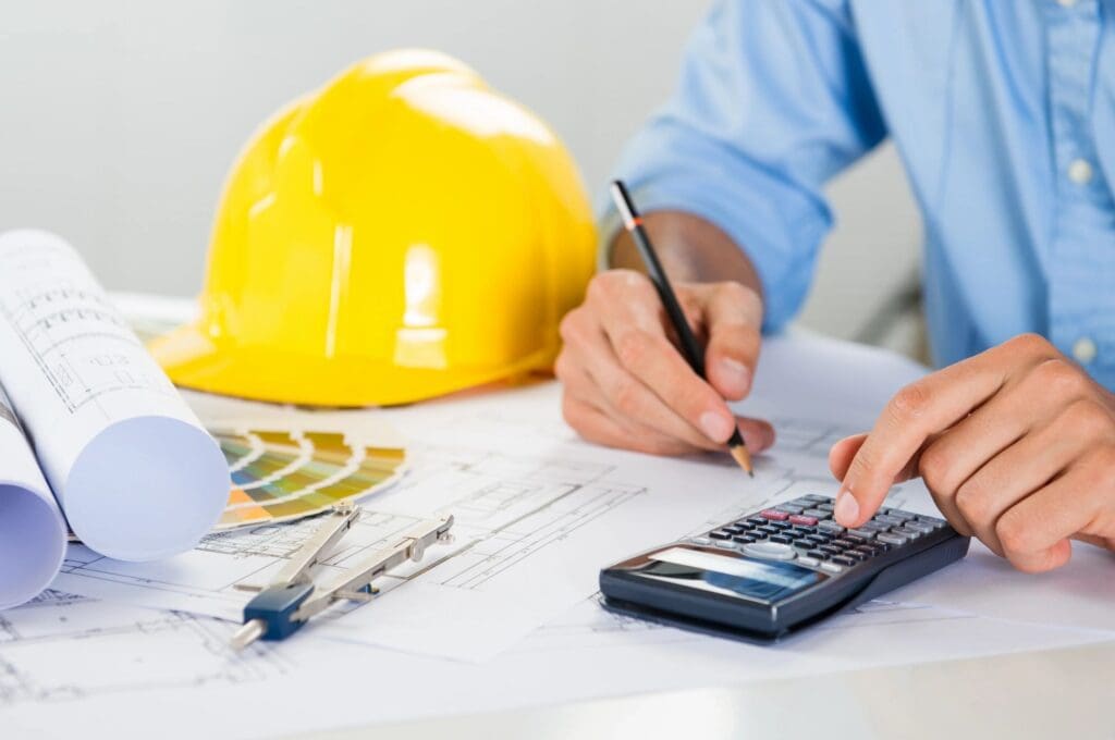A man with a hard hat and calculator working on construction plans.