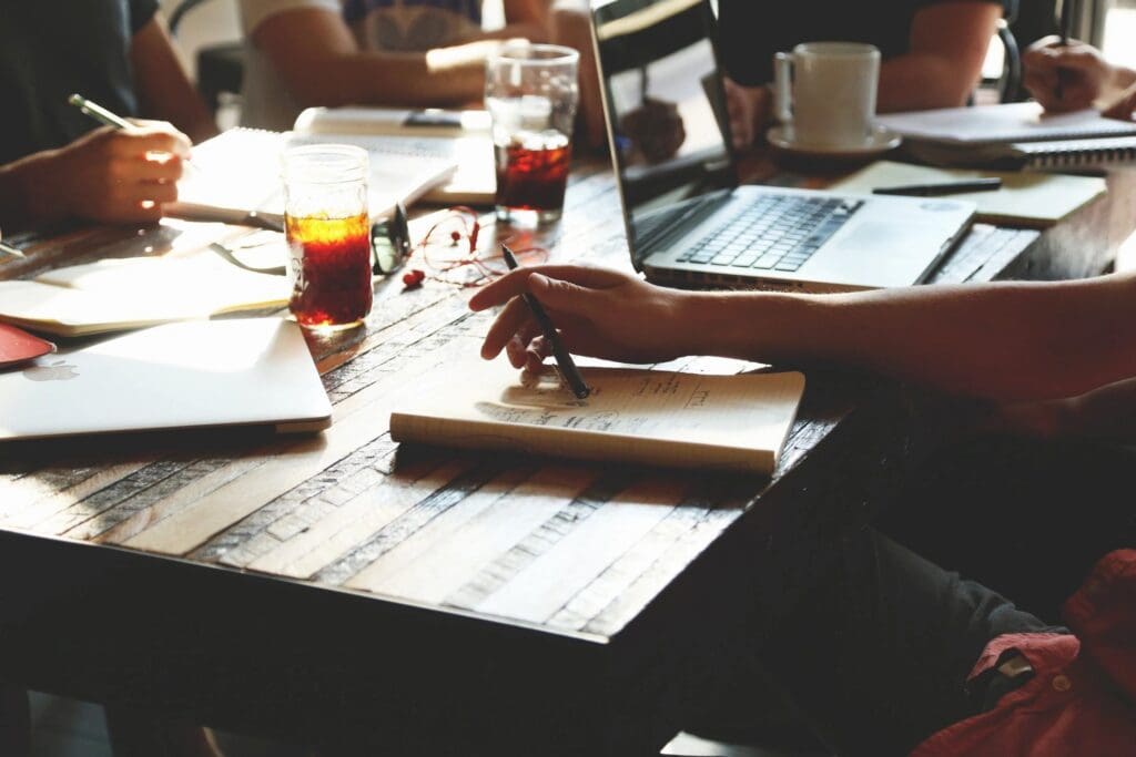 A group of people sitting around a table with laptops and notebooks.