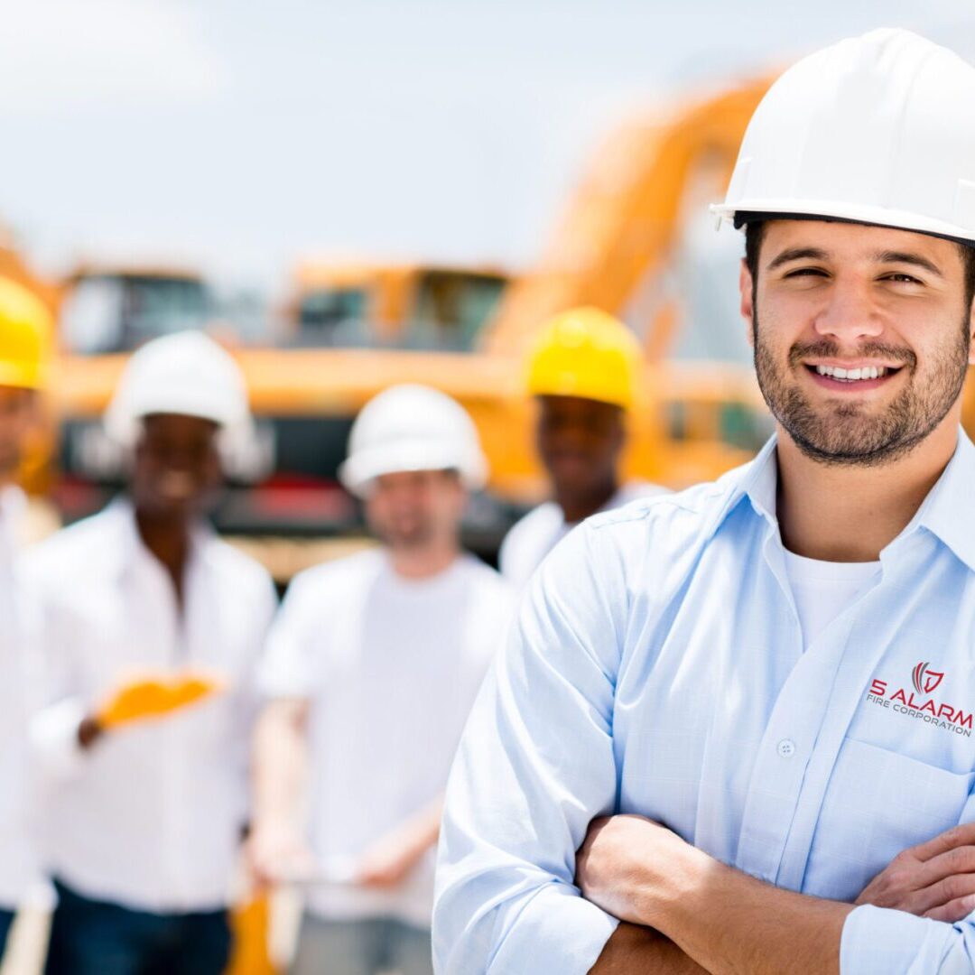 A group of construction workers standing in front of a construction site, ensuring fire alarm services are implemented.