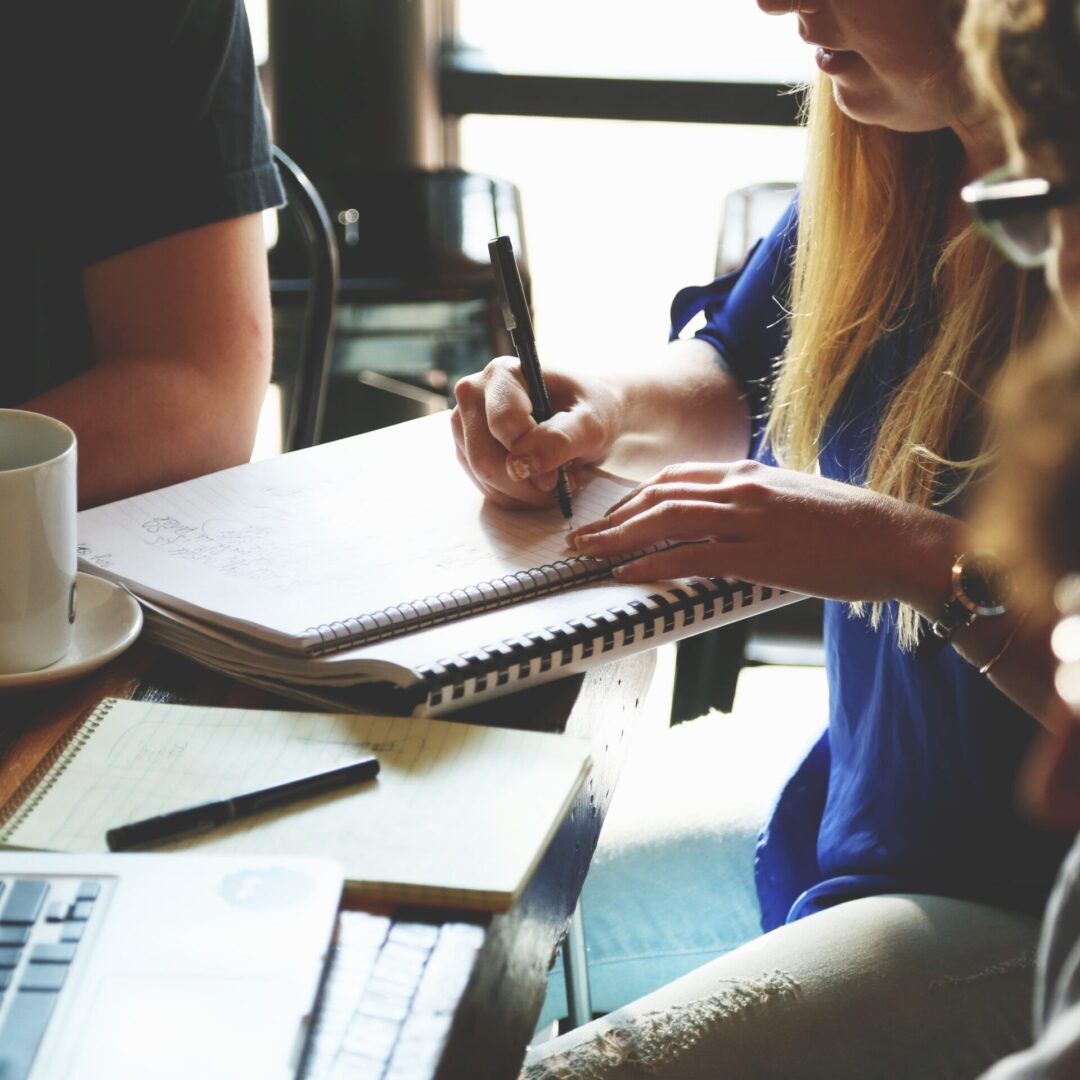 A group of people sitting around a table and writing on a notebook.