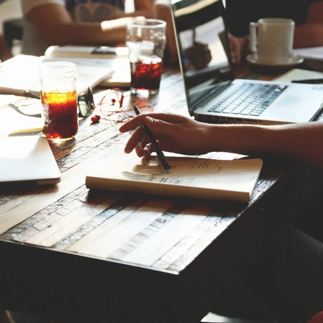 A group of people sitting around a table with laptops and notebooks.