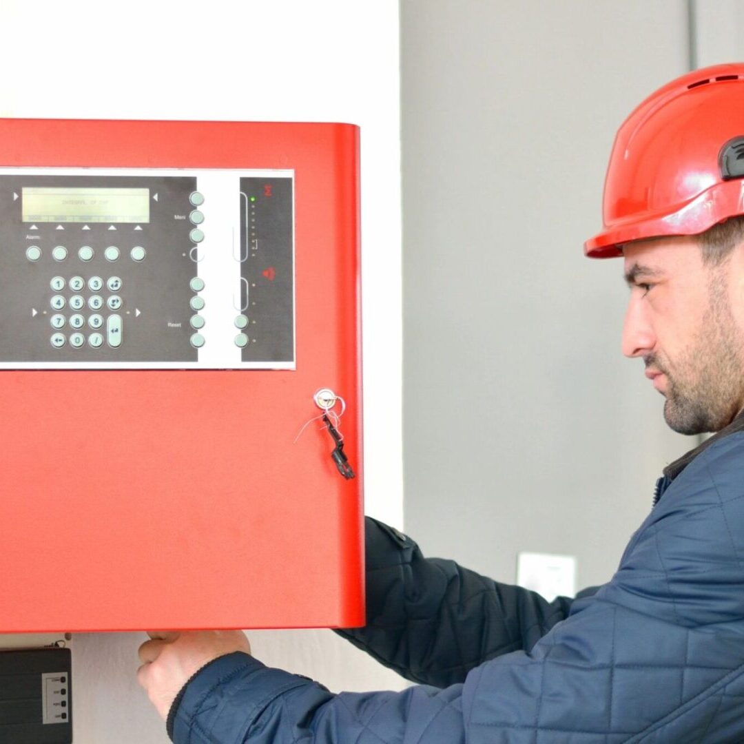 A man in a hard hat is working on a fire alarm.